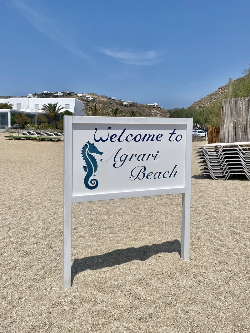 A sign for Agrari Beach stands on a sandy shore in Paralia Agrari, Mykonos.