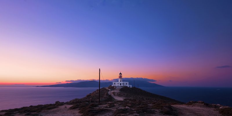 A lighthouse stands tall on a rocky cliff overlooking the Aegean Sea in Armenistis, Mykonos.