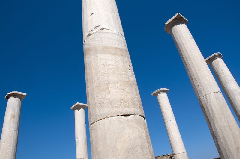 Ancient ruins and columns scattered across the sunlit landscape of Delos, Greece.