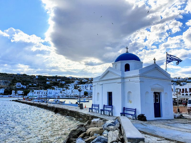 The blue-domed chapel on the Mykonos harbour pier where boat tours set off, with small boats moored behind it