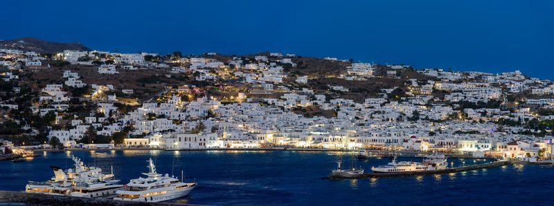 A vibrant Mykonos harbor bustling with nightlife, illuminated by colorful lights.