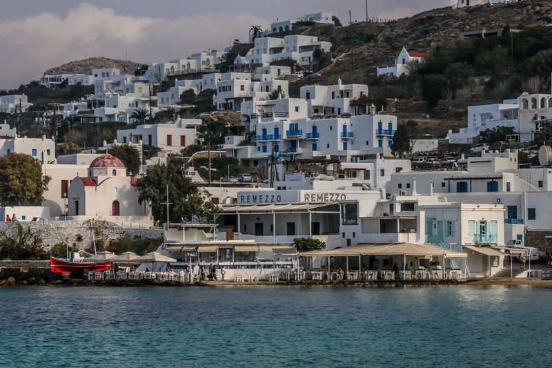 A boat cruises along the scenic South Coast of Mykonos, Greece, with passengers enjoying the view.