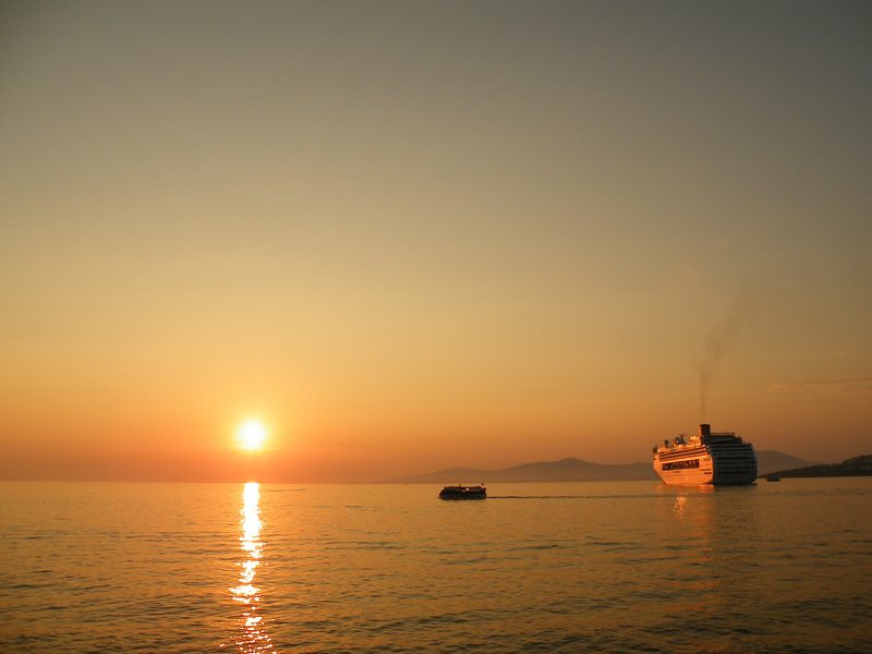 A cruise ship and tender boat at sunset in Mykonos, Greece.