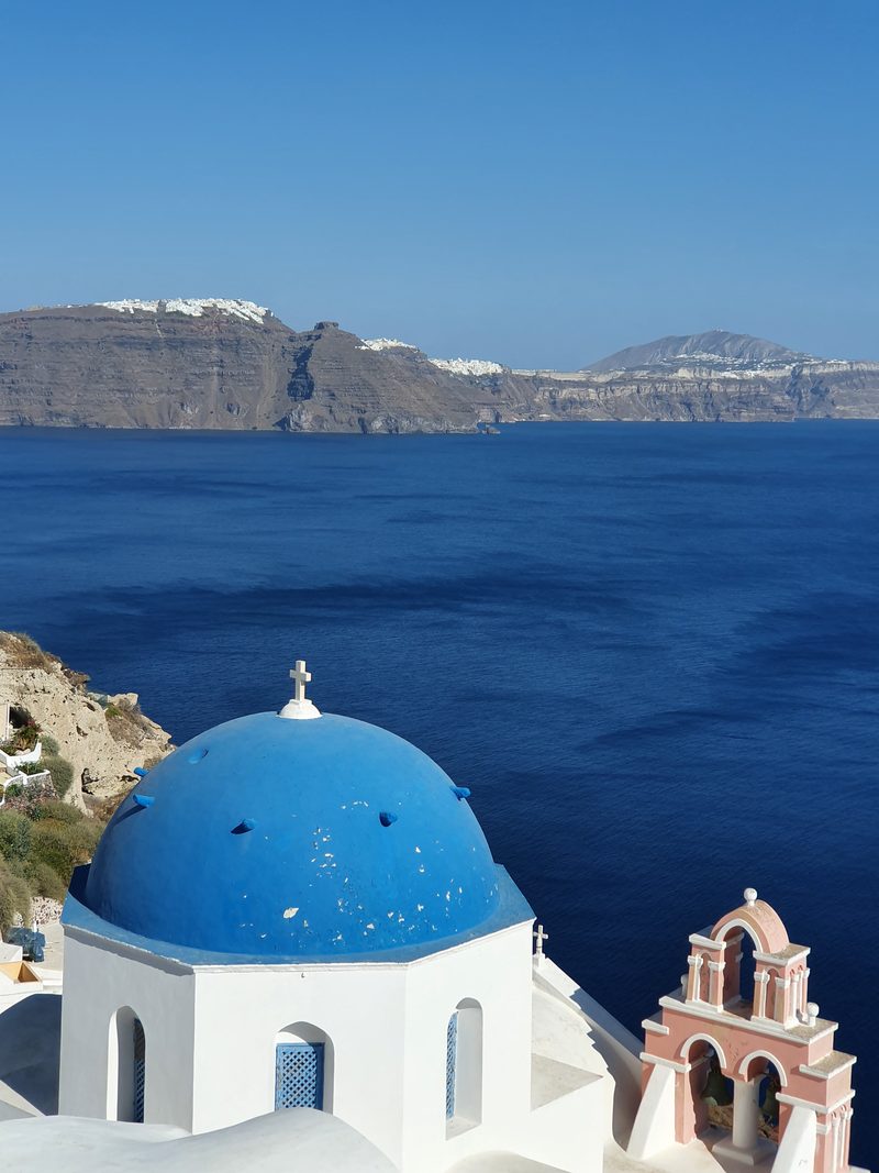 The wide sweep of the Santorini caldera seen from a clifftop church, with the volcanic rim stretching across the deep blue water