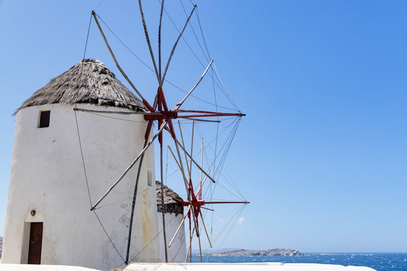 Iconic windmills with white blades stand tall against the blue sky in Mykonos, Greece.