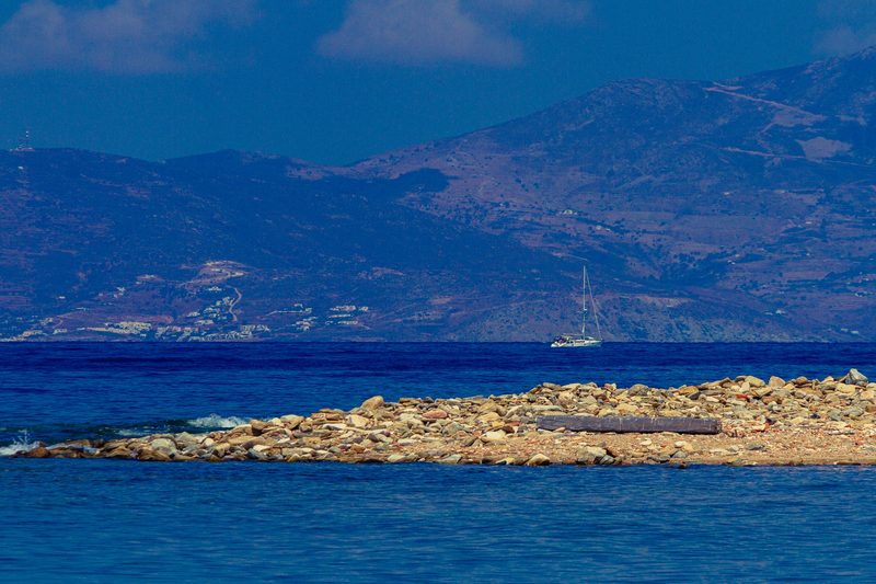 A serene beach scene with clear blue waters and scattered rocks on the Greek island of Delos.