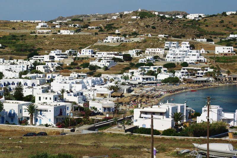 A serene view of Ornos Beach in Mykonos with calm waters and a sandy shore.