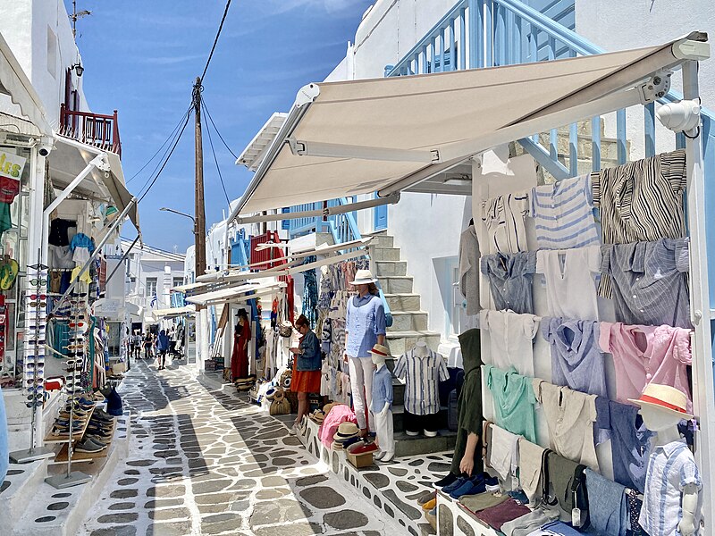Narrow shopping street in Mykonos Town with whitewashed Cycladic buildings, colorful boutiques, and distinctive stone-paved walkway