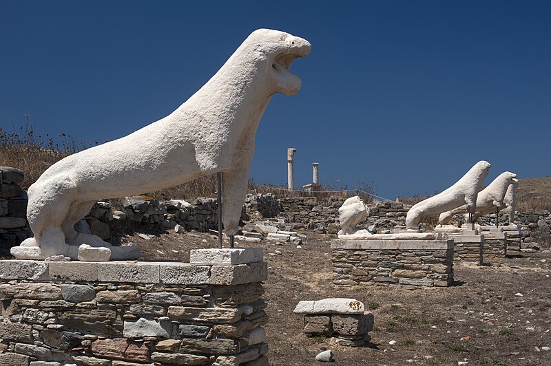 Marble lion statues along the Terrace of the Lions on the ancient island of Delos with stone ruins and columns in the background
