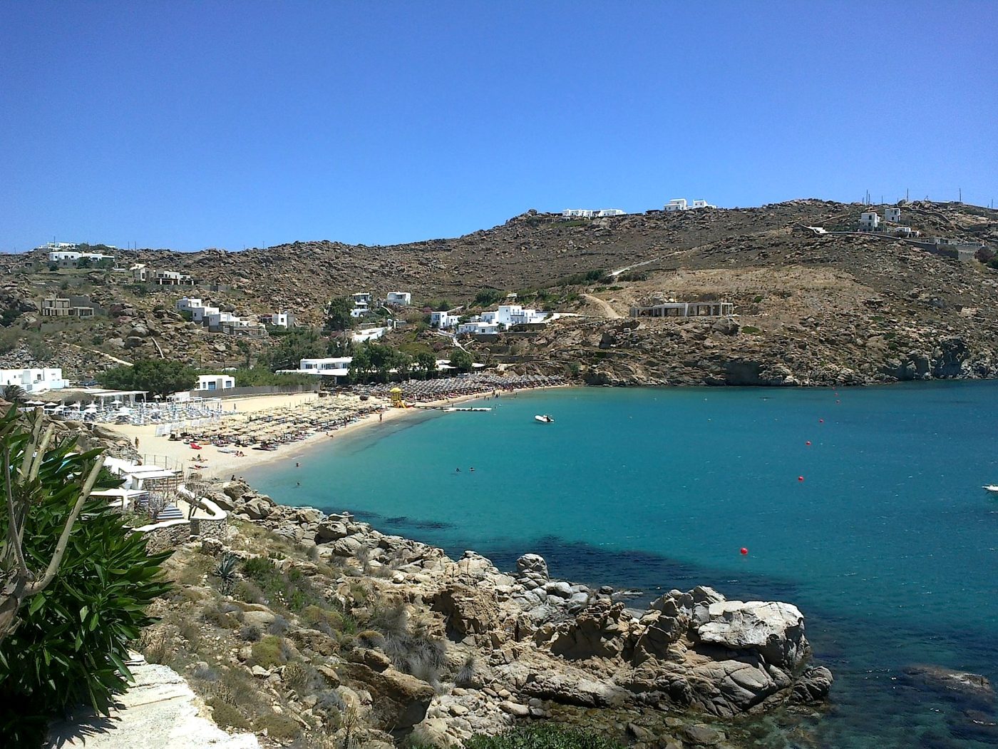 A Mykonos beach with dark sand and clear water typical of the south coast